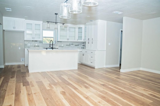 kitchen with hanging light fixtures, light wood-type flooring, an island with sink, decorative backsplash, and white cabinets