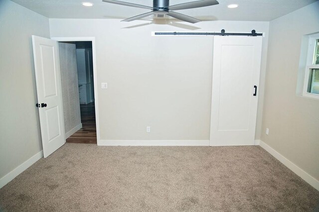 unfurnished bedroom with ceiling fan, a barn door, and carpet floors