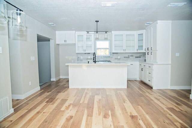 kitchen featuring hanging light fixtures, tasteful backsplash, light hardwood / wood-style floors, white cabinets, and a center island with sink