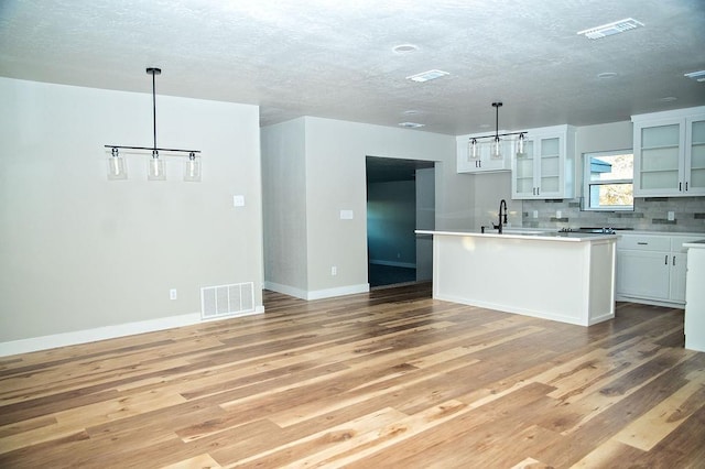 kitchen with a kitchen island with sink, pendant lighting, white cabinets, and light hardwood / wood-style flooring