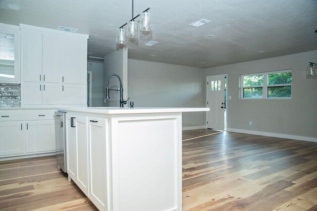 kitchen featuring sink, white cabinetry, light hardwood / wood-style flooring, an island with sink, and pendant lighting