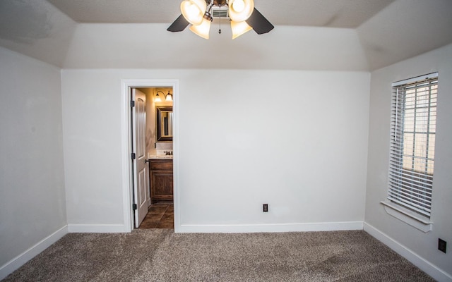 unfurnished bedroom featuring ceiling fan, ensuite bathroom, lofted ceiling, and dark colored carpet