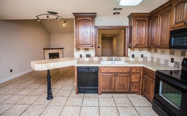 kitchen with sink, tasteful backsplash, light tile patterned floors, a tile fireplace, and black appliances