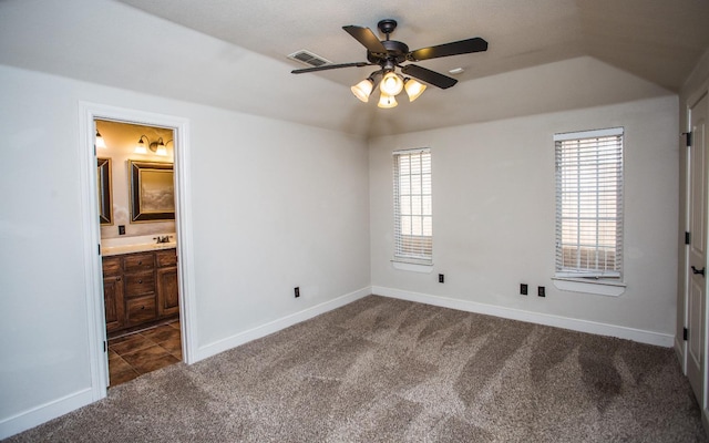 unfurnished bedroom featuring ceiling fan, ensuite bathroom, sink, and dark carpet