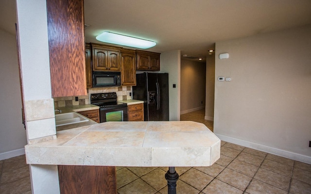 kitchen featuring sink, light tile patterned floors, black appliances, decorative backsplash, and kitchen peninsula