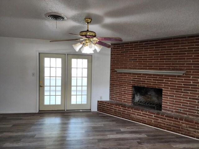 unfurnished living room with ceiling fan, a brick fireplace, a textured ceiling, and dark hardwood / wood-style flooring