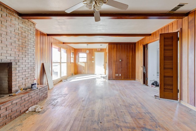 unfurnished living room featuring ceiling fan, light wood-type flooring, beam ceiling, and wood walls