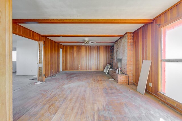 spare room featuring a healthy amount of sunlight, a fireplace, beam ceiling, and wood walls