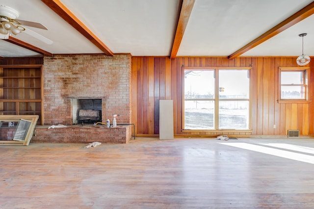 unfurnished living room with plenty of natural light, wooden walls, hardwood / wood-style floors, and beam ceiling