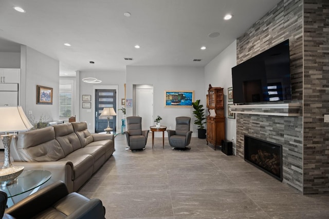 living area featuring a stone fireplace, visible vents, and recessed lighting