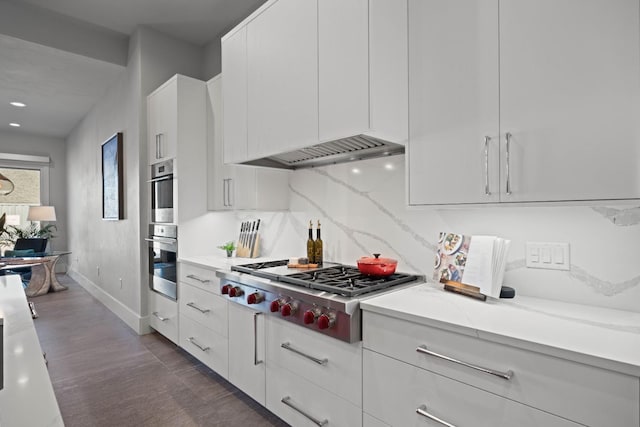 kitchen featuring white cabinetry, light stone counters, wall chimney range hood, stainless steel appliances, and backsplash