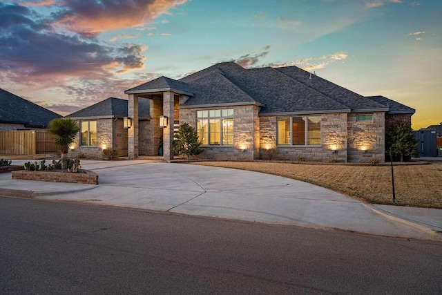 view of front of property with a shingled roof, concrete driveway, fence, and stone siding