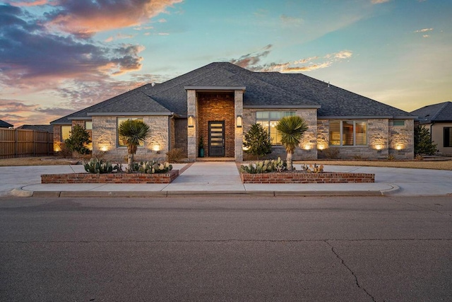 view of front facade with stone siding, fence, and concrete driveway