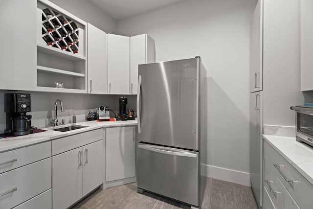 kitchen featuring open shelves, freestanding refrigerator, white cabinetry, a sink, and baseboards