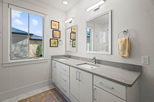 bathroom featuring double vanity, a sink, baseboards, and walk in shower