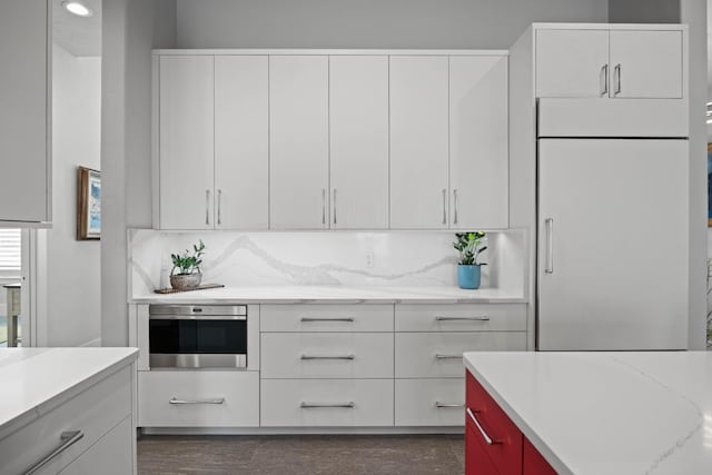 kitchen with white built in fridge, white cabinetry, decorative backsplash, and oven