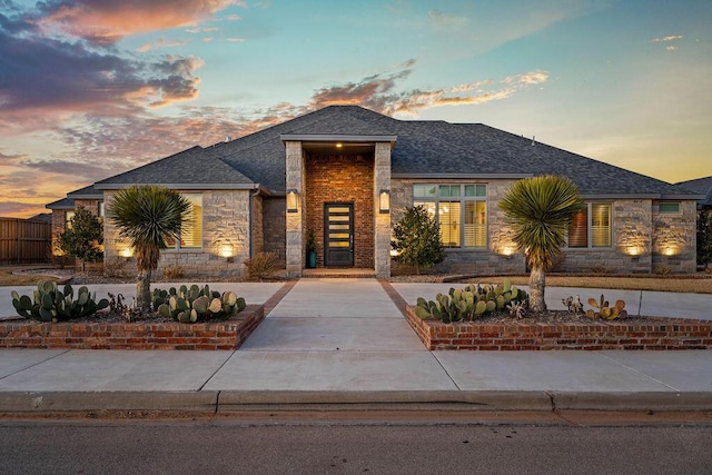 view of front facade featuring stone siding, roof with shingles, and driveway