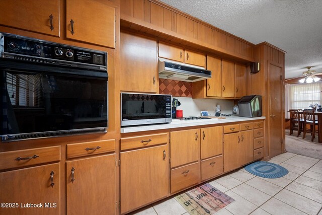 5426 28th St, Lubbock, TX 79407 - kitchen featuring black oven, under cabinet range hood, a textured ceiling, light tile patterned floors, and ceiling fan