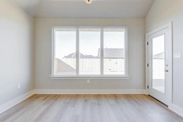 empty room with lofted ceiling, plenty of natural light, and light hardwood / wood-style flooring