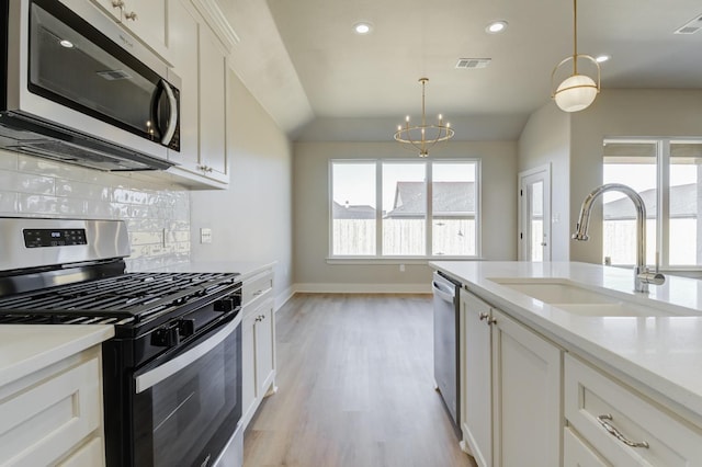 kitchen featuring pendant lighting, sink, white cabinets, light hardwood / wood-style floors, and stainless steel appliances