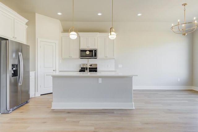 kitchen featuring hanging light fixtures, stainless steel appliances, an island with sink, and white cabinets