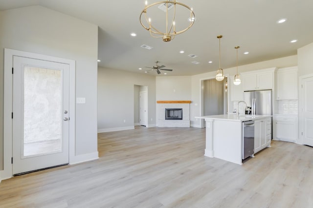 kitchen with white cabinetry, hanging light fixtures, stainless steel appliances, a center island with sink, and a brick fireplace