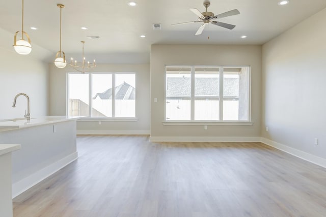 unfurnished living room with ceiling fan with notable chandelier, plenty of natural light, light hardwood / wood-style floors, and sink