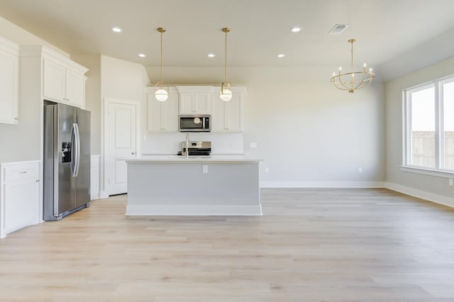 kitchen with white cabinetry, light wood-type flooring, an island with sink, pendant lighting, and stainless steel appliances