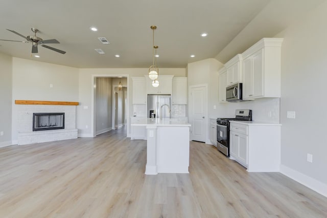 kitchen featuring decorative light fixtures, white cabinets, decorative backsplash, stainless steel appliances, and a center island with sink