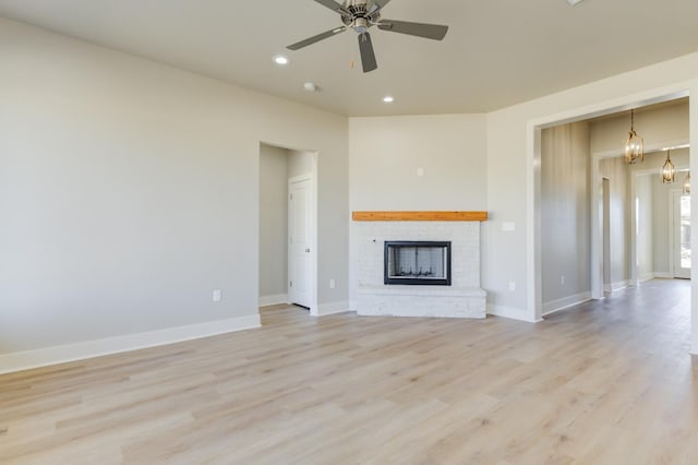 unfurnished living room with a brick fireplace, ceiling fan with notable chandelier, and light hardwood / wood-style floors