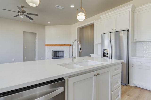 kitchen with sink, tasteful backsplash, a brick fireplace, stainless steel appliances, and white cabinets