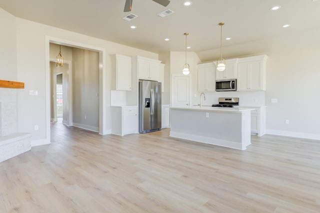 kitchen featuring pendant lighting, appliances with stainless steel finishes, an island with sink, white cabinets, and light wood-type flooring