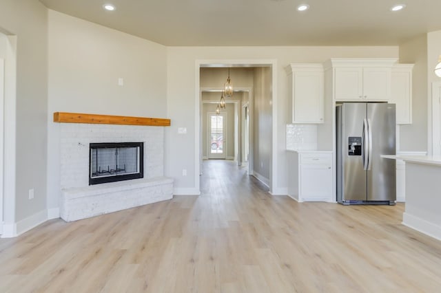 kitchen featuring white cabinetry, decorative backsplash, stainless steel fridge with ice dispenser, a brick fireplace, and light hardwood / wood-style flooring