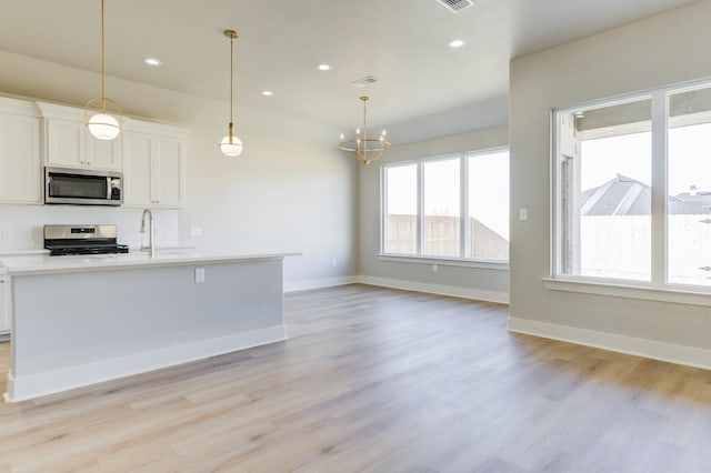 kitchen featuring white cabinetry, an island with sink, pendant lighting, stainless steel appliances, and light hardwood / wood-style floors