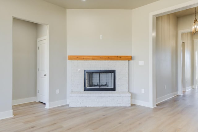 unfurnished living room featuring light wood-type flooring, a brick fireplace, and a notable chandelier