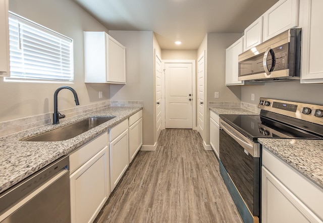 kitchen featuring stainless steel appliances, white cabinetry, hardwood / wood-style flooring, and sink