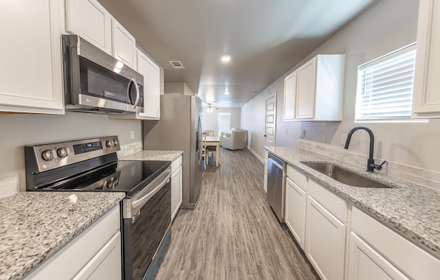 kitchen featuring sink, wood-type flooring, stainless steel appliances, light stone countertops, and white cabinets