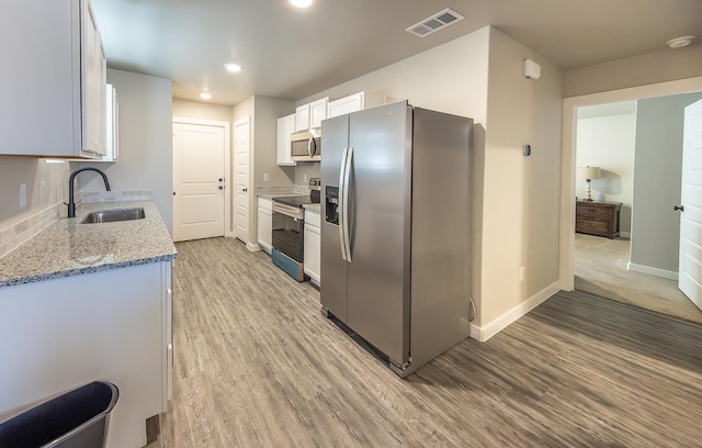 kitchen with appliances with stainless steel finishes, sink, white cabinets, light stone countertops, and light hardwood / wood-style flooring