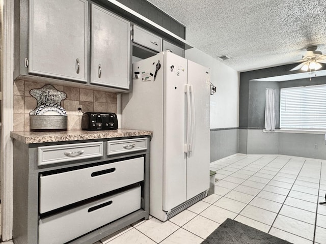 kitchen featuring ceiling fan, white refrigerator, a textured ceiling, light tile patterned flooring, and decorative backsplash