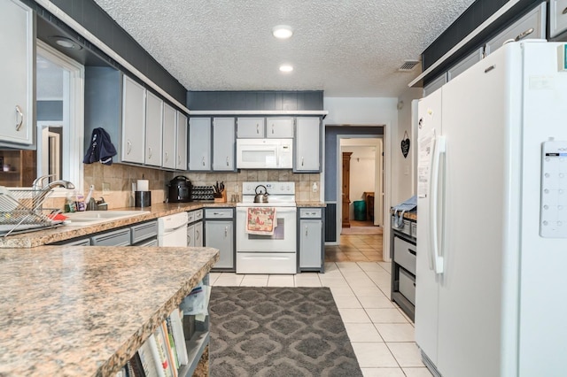 kitchen with gray cabinets, light tile patterned flooring, sink, white appliances, and a textured ceiling