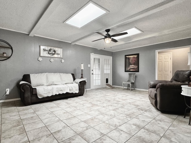 living room featuring a skylight, a textured ceiling, ornamental molding, ceiling fan, and beam ceiling