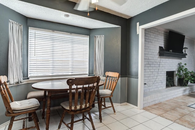 dining room featuring ceiling fan, a brick fireplace, light tile patterned floors, and a textured ceiling