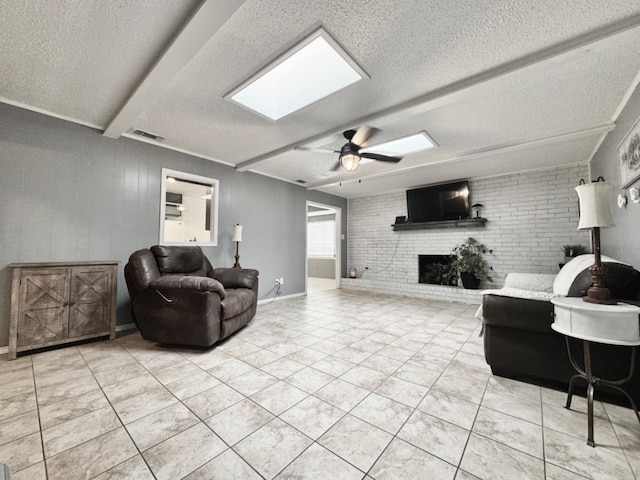 tiled living room with beamed ceiling, a brick fireplace, a textured ceiling, and a skylight