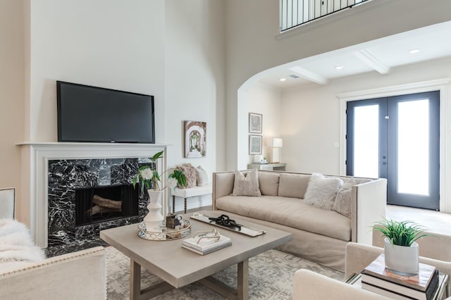 living room featuring french doors, a premium fireplace, and beam ceiling