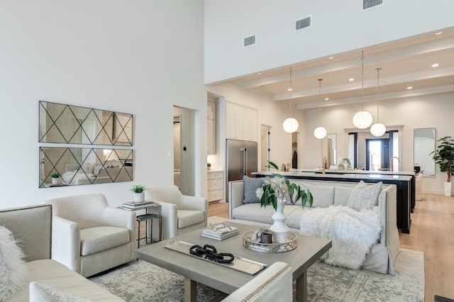 living room featuring a high ceiling, light hardwood / wood-style floors, and beam ceiling