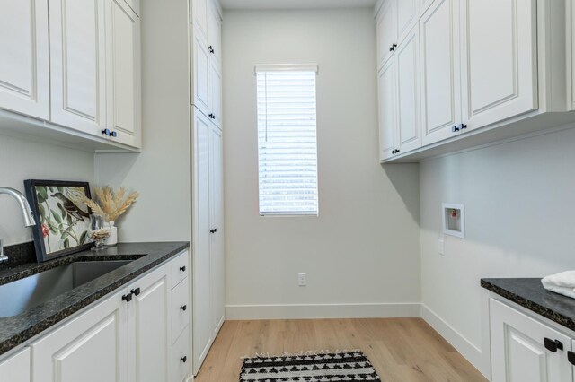 clothes washing area featuring cabinets, sink, washer hookup, and light hardwood / wood-style floors