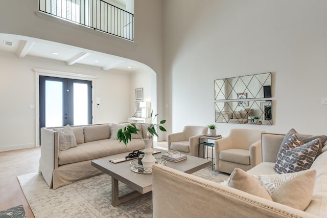 living room with french doors, beam ceiling, light hardwood / wood-style floors, and a high ceiling