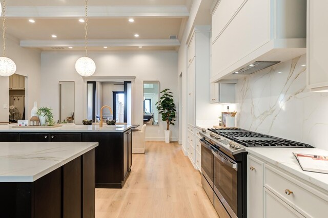 kitchen with gas range, light stone counters, decorative light fixtures, an island with sink, and white cabinets