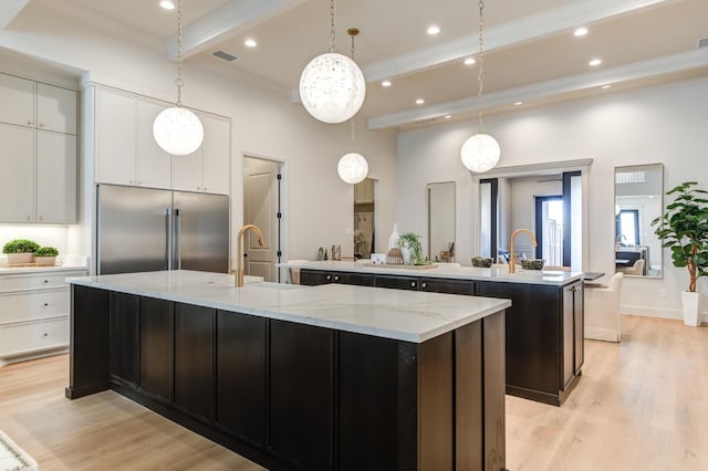 kitchen featuring built in refrigerator, white cabinets, and a large island with sink