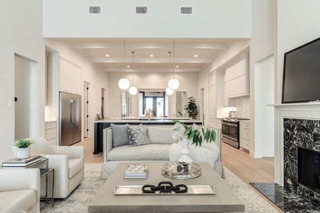 living room with light hardwood / wood-style flooring, beam ceiling, and a high end fireplace